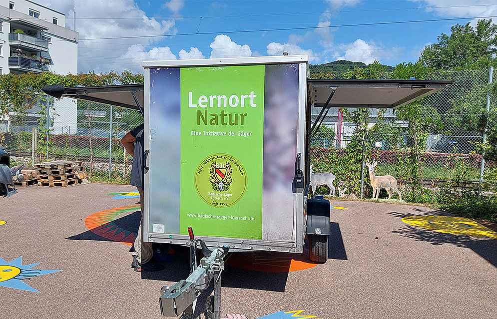 Jäger Max Vogel zu Besuch an der Schöpflin Schule mit seinem Info-Mobil »Lernort Natur«, Zu sehen ist ein Autoanhänger auf dem steht: Lernort Natur 